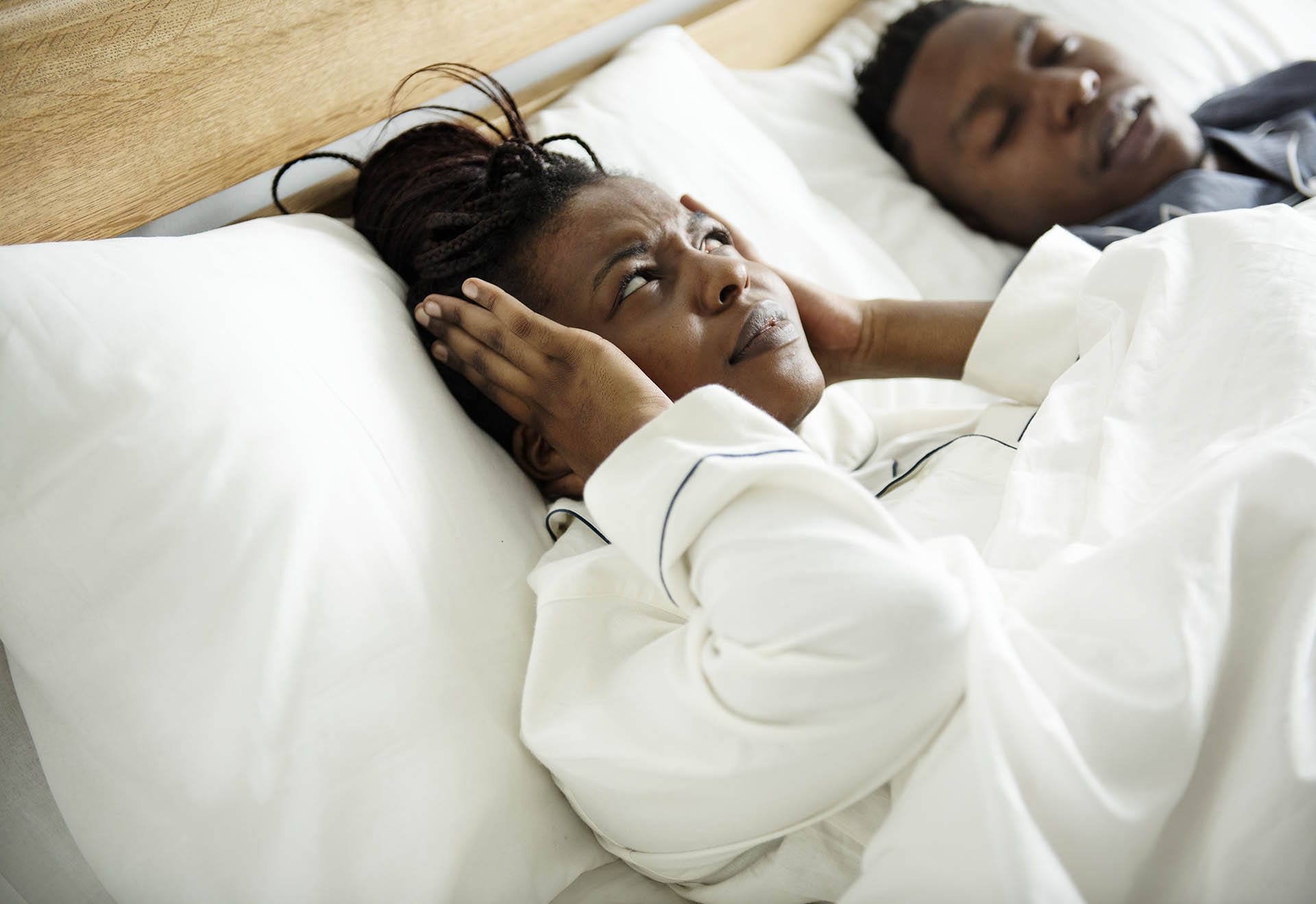 Woman covering her ears while her husband snores in bed