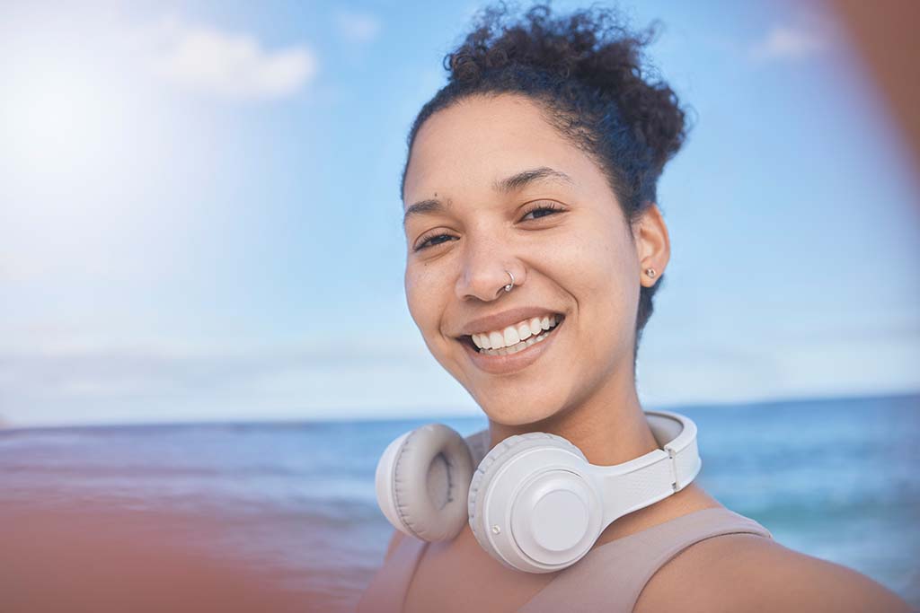 Young woman from Fair Oaks, CA who strive for optimum health walking on the beach with her headphones taking a selfie