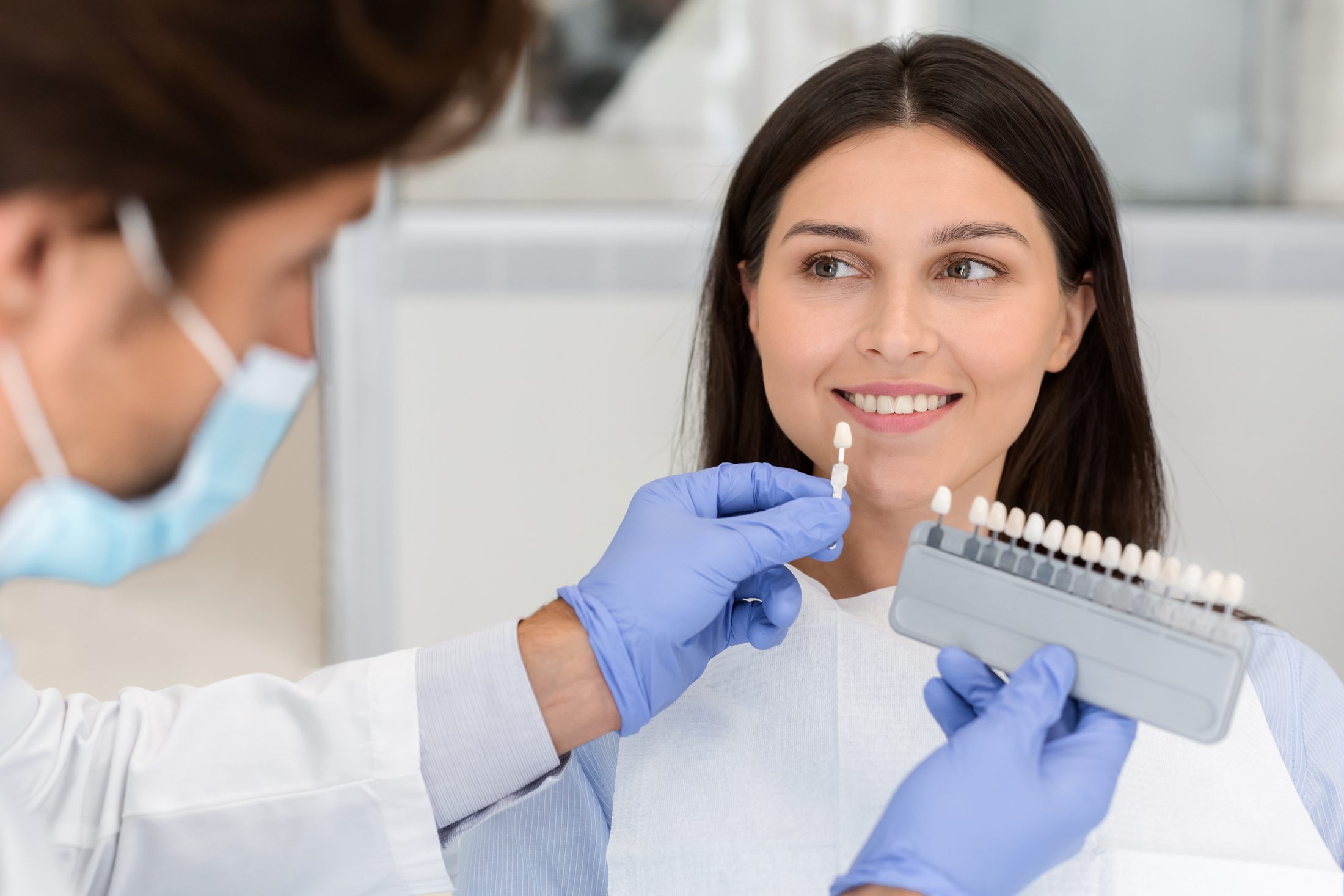 Veneers vs. Bonding Dentist applying sample from tooth scale to smiling patient teeth