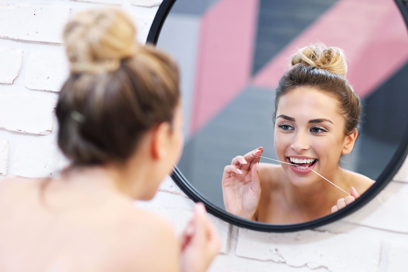 woman flossing her teeth in front of bathroom mirror